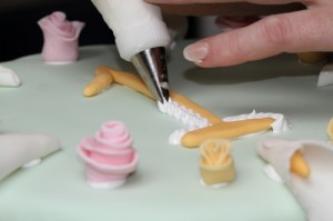 piping decorative icing, on fondant covered cake decorated with calla lilies and roses, photo by LdV of www.laurens.com